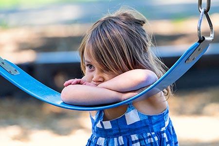 Troubled unhappy child whose birth parents may have bipolar disorder leans on swing seat