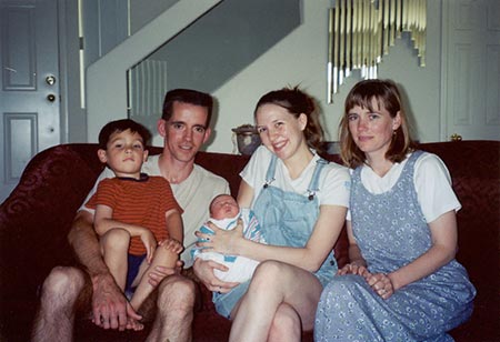 an adoptive family of 5 pose together with their newly adopted baby on a couch 