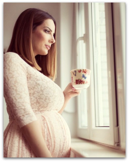 pregnant woman sipping tea while looking out the window