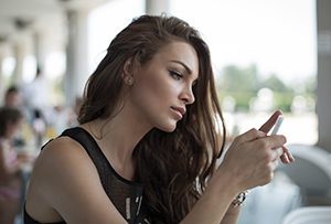 Young woman sitting in restaurant looking at smartphone considering if adoption is right for her