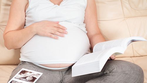 Cropped photo of pregnant woman reading a book, ultrasound photo on her lap