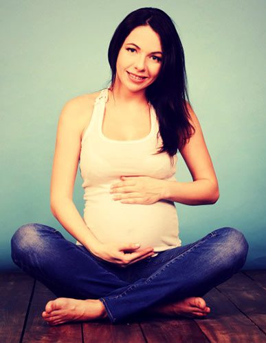 Young pregnant woman sitting on the ground, wearing a tank and jeans