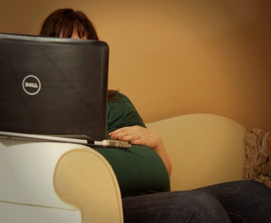 heavily pregnant woman browsing the Internet on a laptop