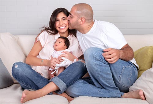 Happy young family. Husband kisses wife, who holds their baby