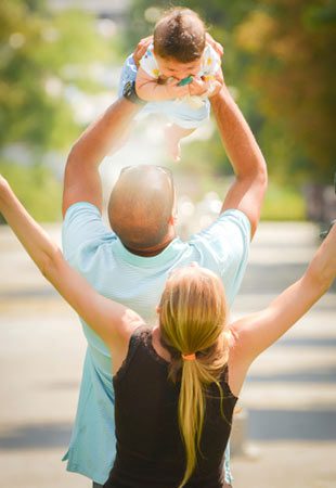 Joyful adoptive parents outdoors, dad lifts the child up in the air