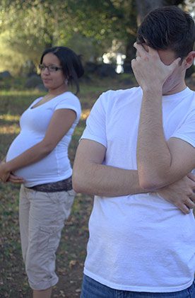 Young man in the foreground hiding his face, young pregnant woman in the background