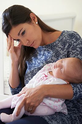 Young woman who looks overwhelmed holds a sleeping infant