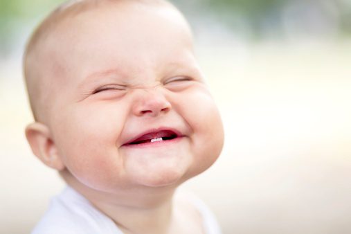 Caucasian baby with a big smile, showing his two bottom teeth
