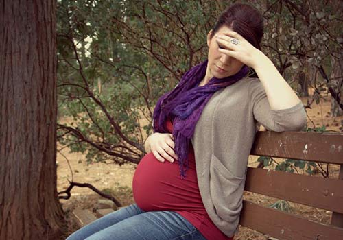 A pregnant woman sits on a park bench, in anguish over a decision