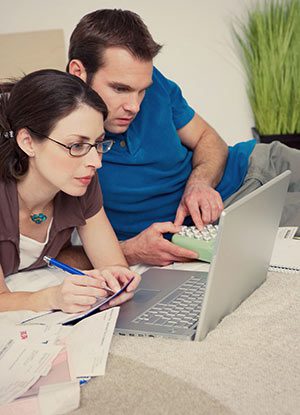 A young couple balances their checkbook while looking at their online statement