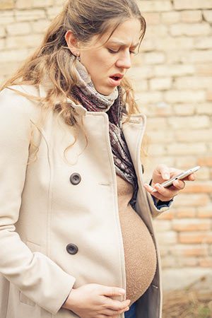 Pregnant woman walking outside, looking down at her phone