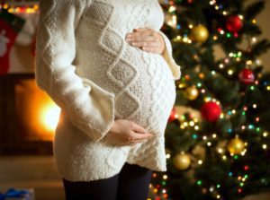 Closeup photo of pregnant woman posing against fireplace and Christmas tree