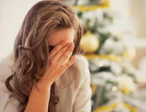 Woman in anguish, with her hand on her face. Christmas tree in the background