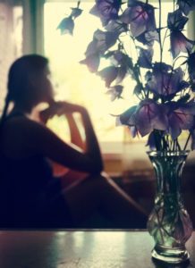Young woman looks out the window, vase of flowers in the foreground
