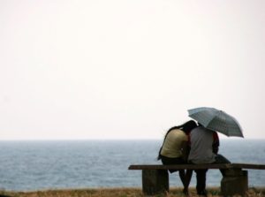 Sad couple sit on a bench by the ocean