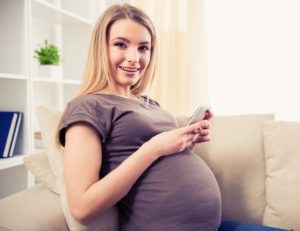 Pregnant woman using her cell phone on sofa