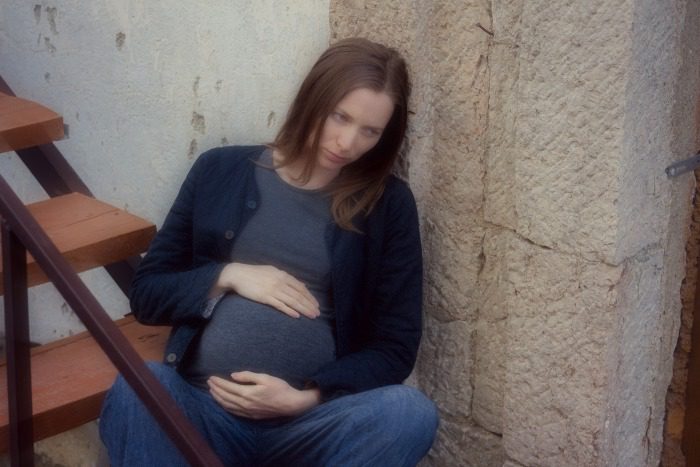 Pregnant woman seated on outdoor steps, worrying because she used drugs during pregnancy