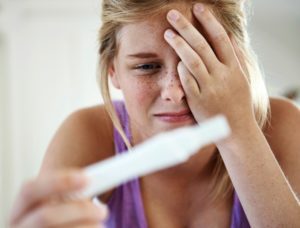 A teenage girl looking dismayed as she sees the result of a pregnancy test