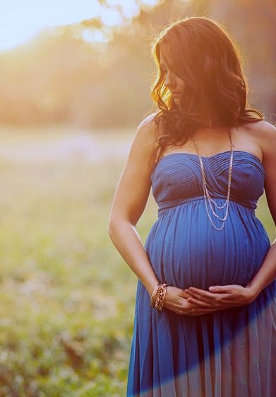 Pregnant woman in a blue dress posing with her hands on her belly