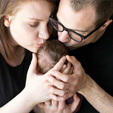 Happy couple kiss their newborn adopted baby