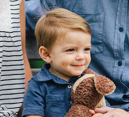 Smiling young boy holding his teddy bear who was adopted through Lifetime