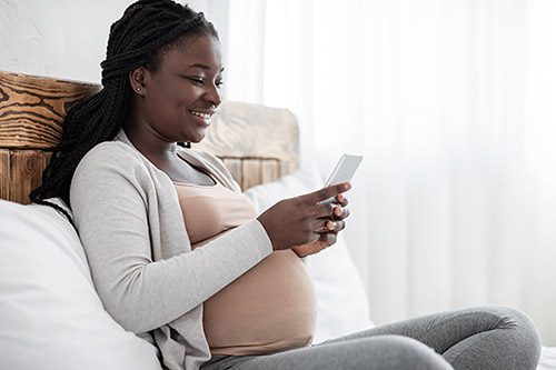 Young pregnant African American woman looking at her phone, choosing adoptive parents for her baby