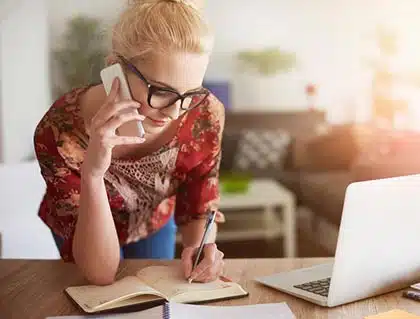 Woman speaking on phone with her coordinator and taking notes about her Lifetime Adoption Profile