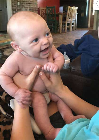 Baby smiling in hands of adoptive parents old enough to adopt