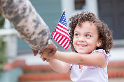 United States active duty father greets his daughter who is holding an American flag and smiling