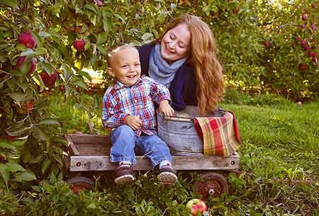 an adopted child sits in cart with barrel of apples while mother looks on