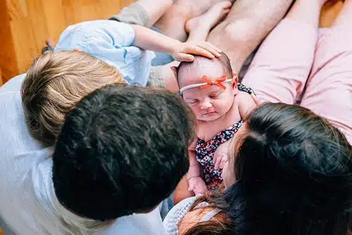 Caucasian parents sitting on a hardwood floor with their firstborn child and a newly adopted infant