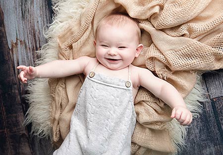 cute baby giggles at the camera while lying on a blanket