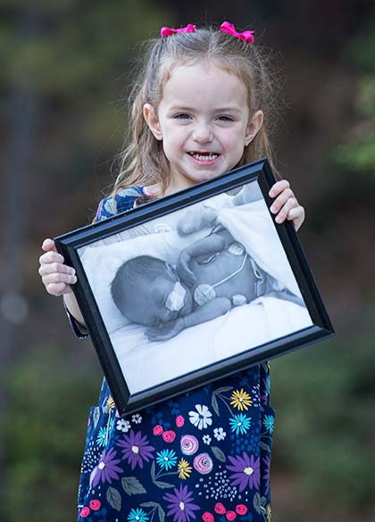 now healthy adopted child who was born with special needs shows off a picture of herself as a baby when she was in the hospital