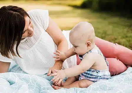 Picture of an adopted new born infant with her adoptive mother on a blanket in a park