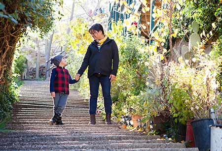 adoptive mom holds her son's hand as they walk along a path discussing adoption together