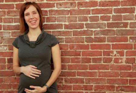 Smiling pregnant woman standing in front of a brick wall