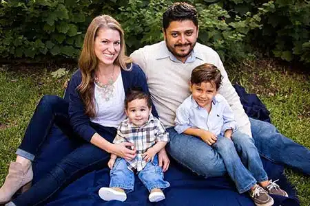 Adoptive parent pose with their two adopted boys sitting on a blanket in the yard