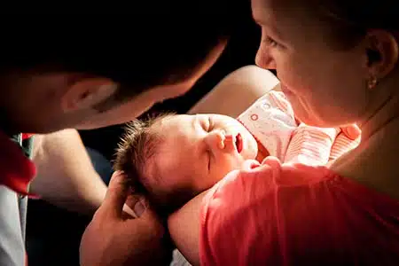 baby sleeps in adoptive mother's arms while dad looks on