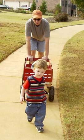 adoptive dad helps his child pull his wagon on a sidewalk