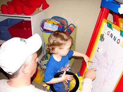 adoptive dad plays with his son as they draw together on an easel