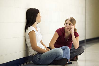 Two young Caucasian women sitting on the floor of a school discussing rape 