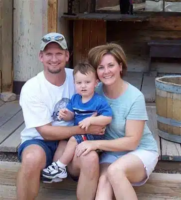 adoptive parents with their son sit outside on the deck and pose for the camera