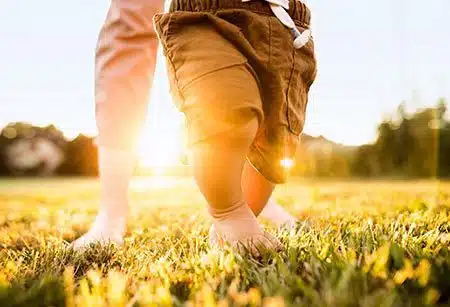 Adoptive mother helps baby walk through the grass