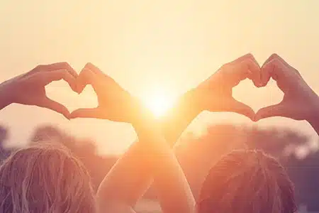 children making hearts with their hands over their heads silhouetted by the sun