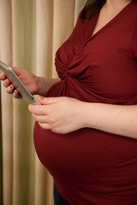 An African American young woman holding her smart phone is pregnant and considering adoption 
