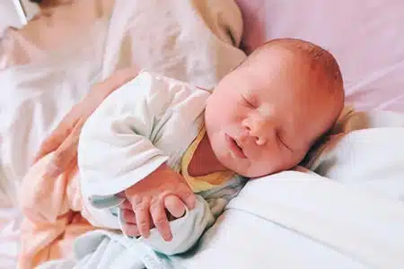 A newborn adopted infant peacefully sleeping in a bed next to a parent