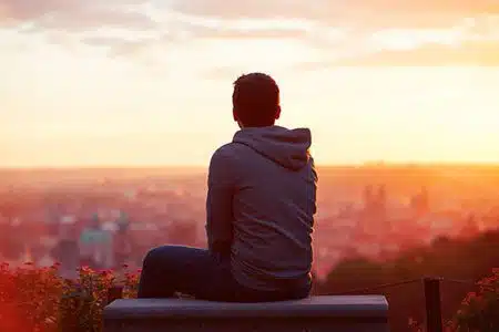man sits on bench looking over city at sunset
