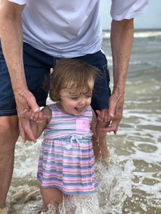 Father helping his happy adopted daughter wade her feet in the ocean