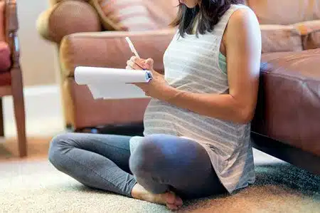 Pregnant woman taking notes while listening to one an adoption podcast