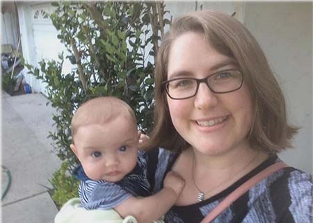 Single adoptive mom stands outside holding her new baby and smiling